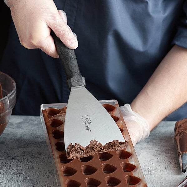 A person using an Ateco stainless steel chocolate scraper to cut chocolate into a tray.