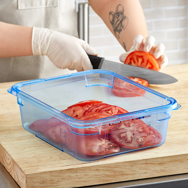 A person cutting tomatoes in a blue Araven plastic food pan.