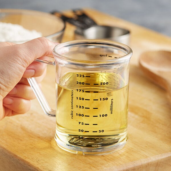 A hand holding a Carlisle polycarbonate measuring cup with yellow liquid.