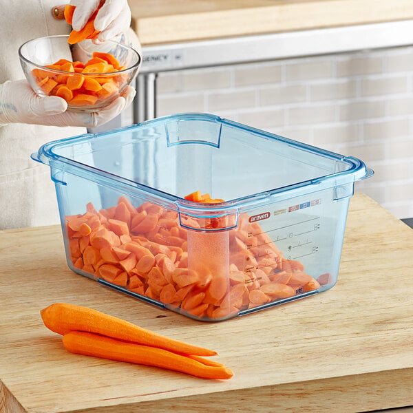 A woman using an Araven blue plastic food container to hold a bowl of cut carrots.