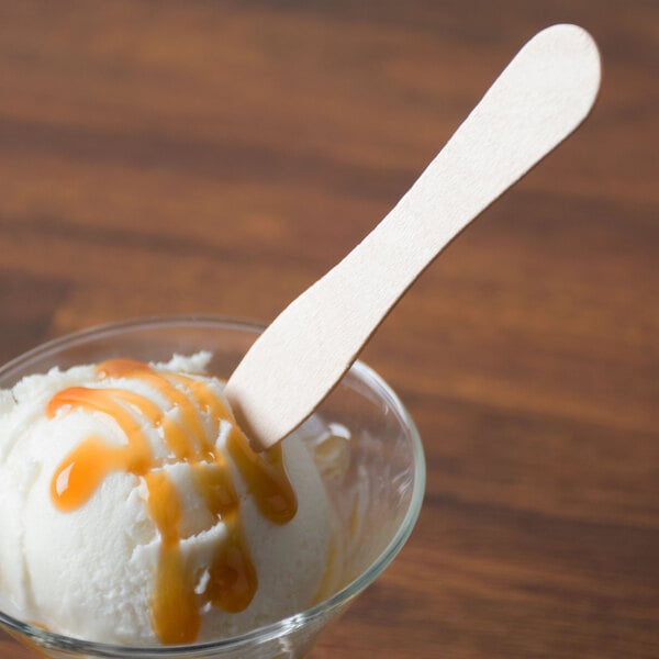 A Royal Paper wooden taster spoon in a glass with a scoop of ice cream and caramel sauce.