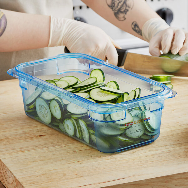 A person cutting cucumbers in an Araven blue plastic food pan.