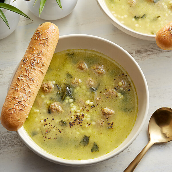 A bowl of Knorr Italian Style Wedding and Meatballs Soup with a spoon and a loaf of bread.
