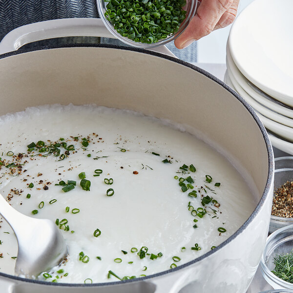 A person pouring LeGout cream soup base into a pot of white soup with green onions.