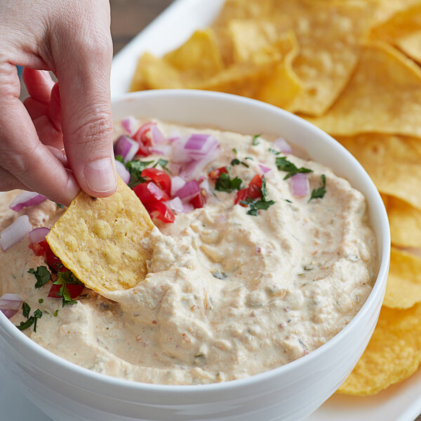 A person dipping a chip into a white bowl of Knorr Chili Con Queso dip.