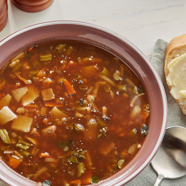 A bowl of Knorr beef flavored vegetable and barley soup with bread and a spoon.