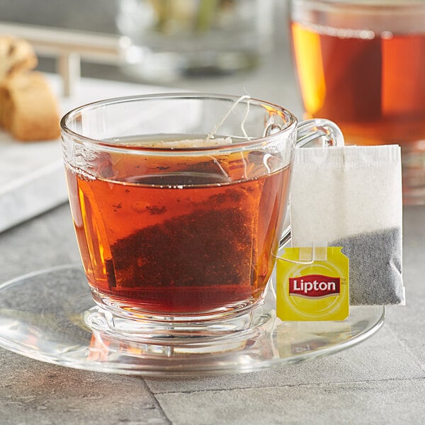 A glass of Lipton classic black tea with a tea bag on a saucer.