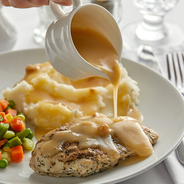 A plate of mashed potatoes and chicken with LeGout chicken gravy being poured on it.