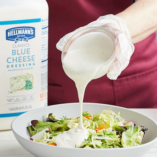 A person pouring Hellmann's Chunky Blue Cheese dressing over a salad.