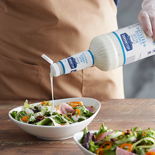 A person pouring Hellmann's blue cheese dressing into a bowl of salad.