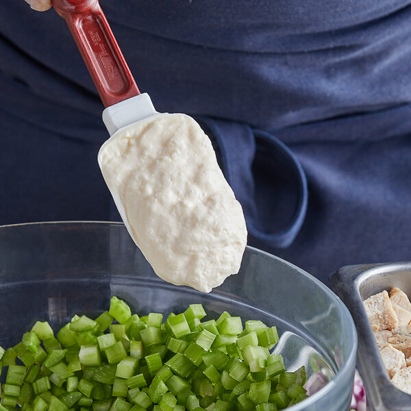 A person using a spatula to spread Hellmann's mayonnaise on a bowl of green onions.