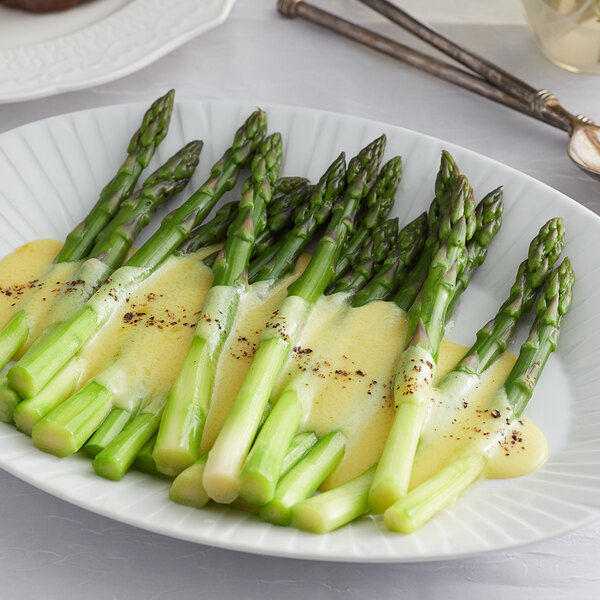A plate of asparagus with Knorr Hollandaise sauce on a white surface.