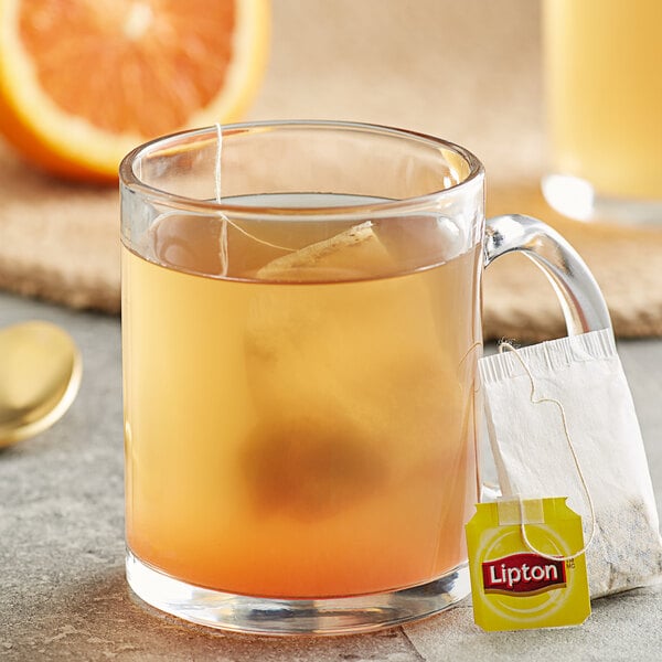 A glass mug of Lipton orange herbal tea with a tea bag in it.