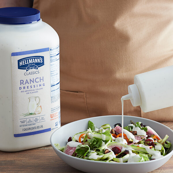A bowl of salad with white sauce being poured into it using Hellmann's Creamy Ranch Dressing.