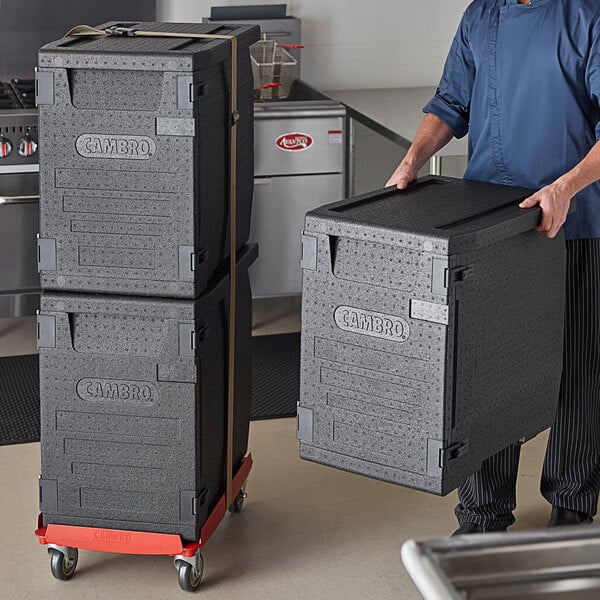 A man using a hot red Cambro Pan Carrier Kit to transport black boxes.