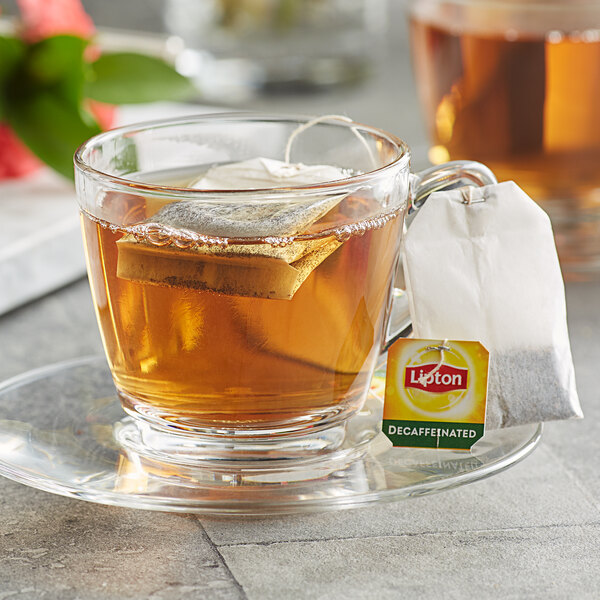 A glass cup of decaffeinated Lipton black tea with a tea bag in it.