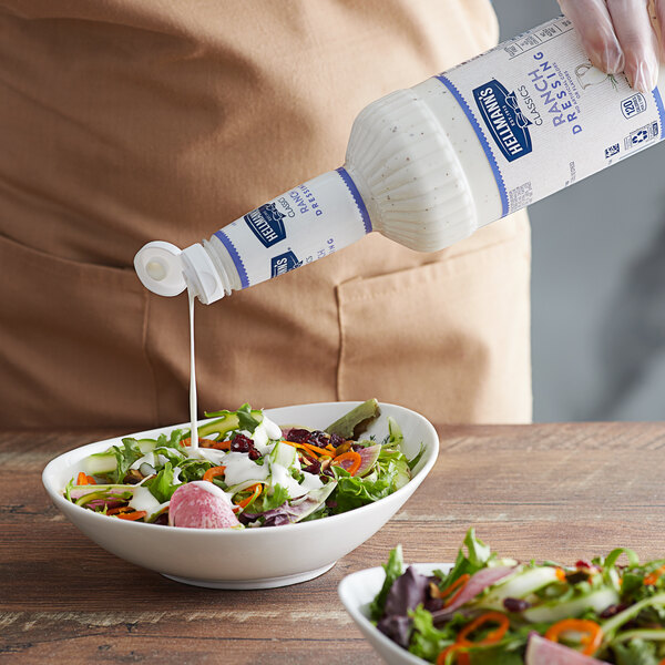 A person pouring Hellmann's Easy Pour Ranch Dressing from a white bottle onto a bowl of salad.
