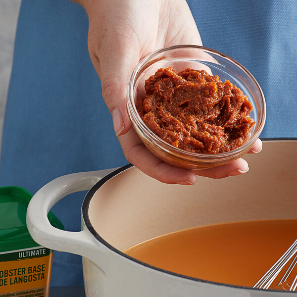 A person holding a bowl of red sauce with Knorr Ultimate Lobster Bouillon Base.