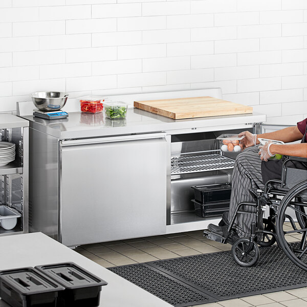 A person in a wheelchair using an Avantco worktop refrigerator in a kitchen.