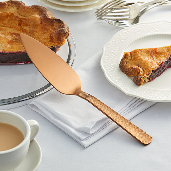 A piece of pie on a plate with an American Metalcraft hammered bronze pie server.