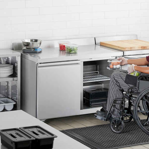 A woman in a wheelchair using an Avantco worktop refrigerator in a professional kitchen.