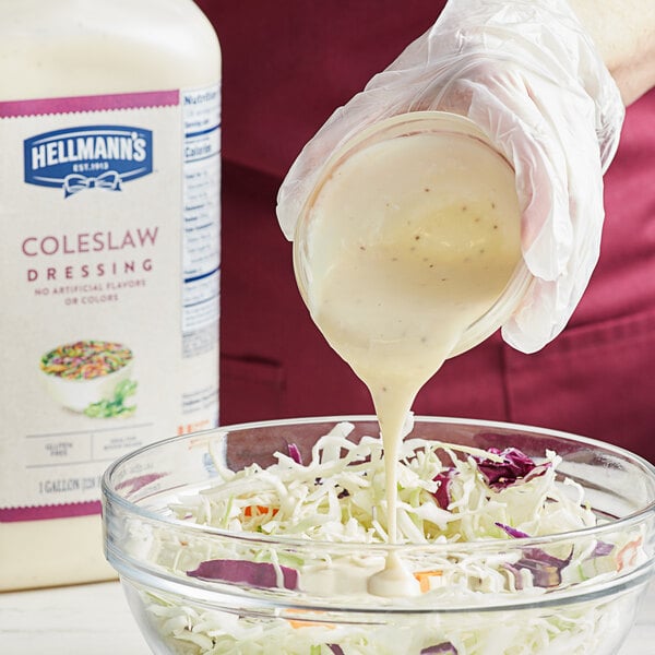 A person pouring Hellmann's creamy coleslaw dressing into a bowl of shredded cabbage.