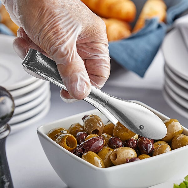 A person using American Metalcraft vintage stainless steel tongs to serve olives from a bowl.