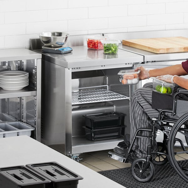A person in a wheelchair in a professional kitchen using an Avantco stainless steel worktop freezer.