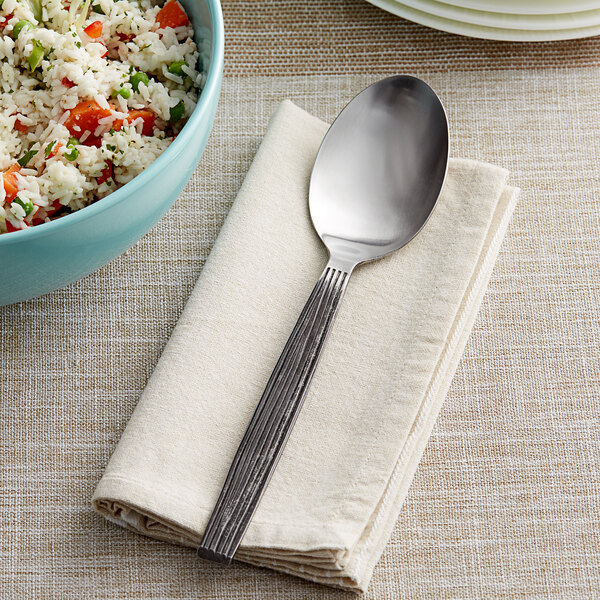 A stainless steel wavy solid spoon on a napkin next to a bowl of rice.