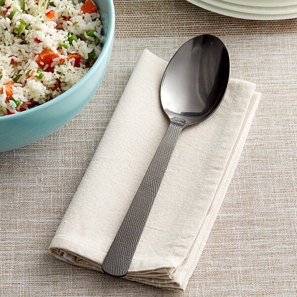 An American Metalcraft hammered black serving spoon on a napkin next to a bowl of rice.