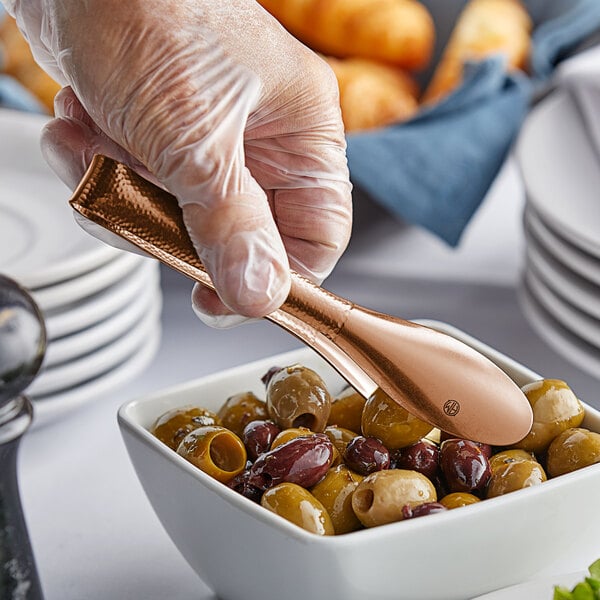 A person using American Metalcraft hammered bronze tongs to serve olives from a bowl.