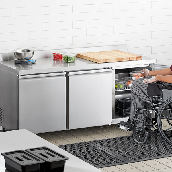 A person in a wheelchair using an Avantco stainless steel worktop refrigerator.