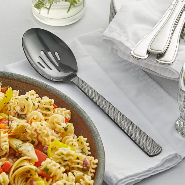 A bowl of pasta with a slotted serving spoon on a table.
