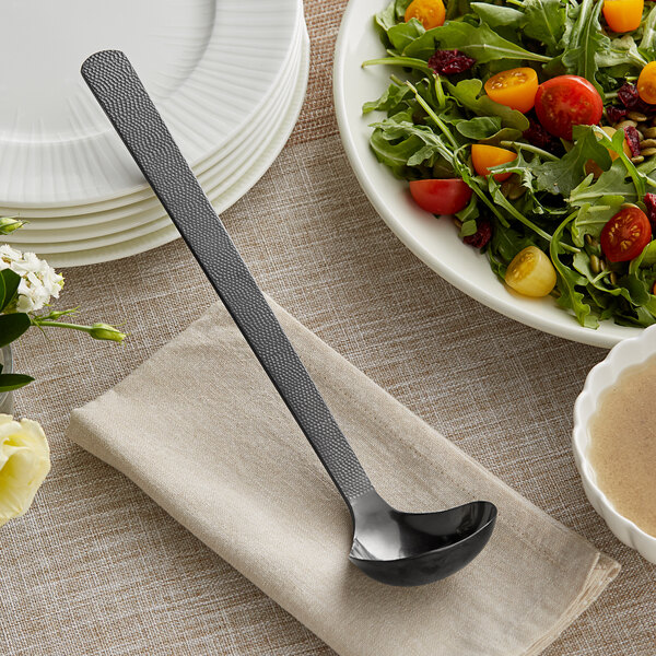 An American Metalcraft hammered black ladle in a bowl of salad with tomatoes and greens.