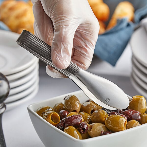 A hand using American Metalcraft stainless steel wavy tongs to serve olives from a bowl.