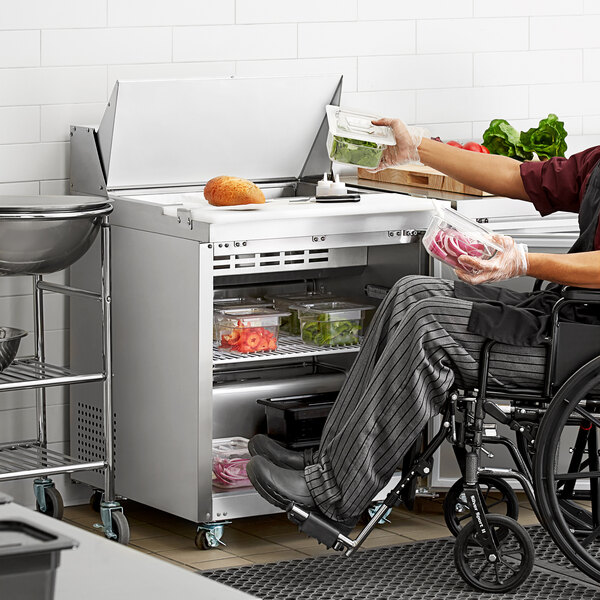 A man in a wheelchair using an Avantco stainless steel refrigerator to prepare food.