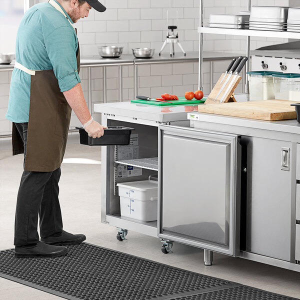 An Avantco stainless steel undercounter freezer on a kitchen counter with a man wearing an apron.