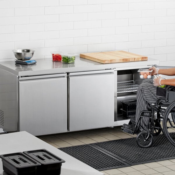 A person in a wheelchair using an Avantco stainless steel undercounter refrigerator.