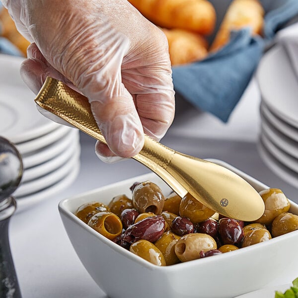 A person holding American Metalcraft hammered gold tongs over a bowl of olives.