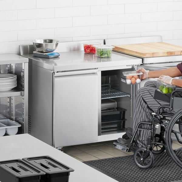 A person in a wheelchair putting limes in an Avantco worktop refrigerator.