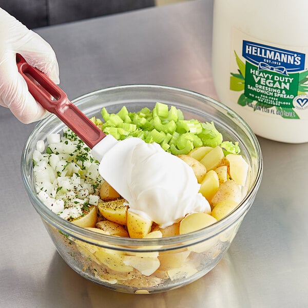 A gloved hand mixes Hellmann's vegan mayonnaise in a bowl of food.