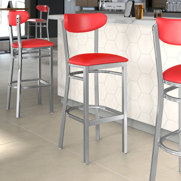 Lancaster Table & Seating Boomerang Series bar stool with red vinyl seat and back on a counter in a cocktail bar.