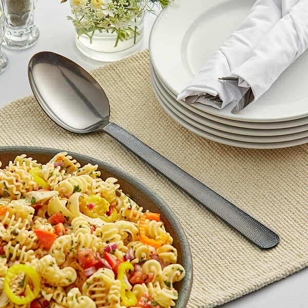 An American Metalcraft hammered black serving spoon on a plate of pasta with vegetables.