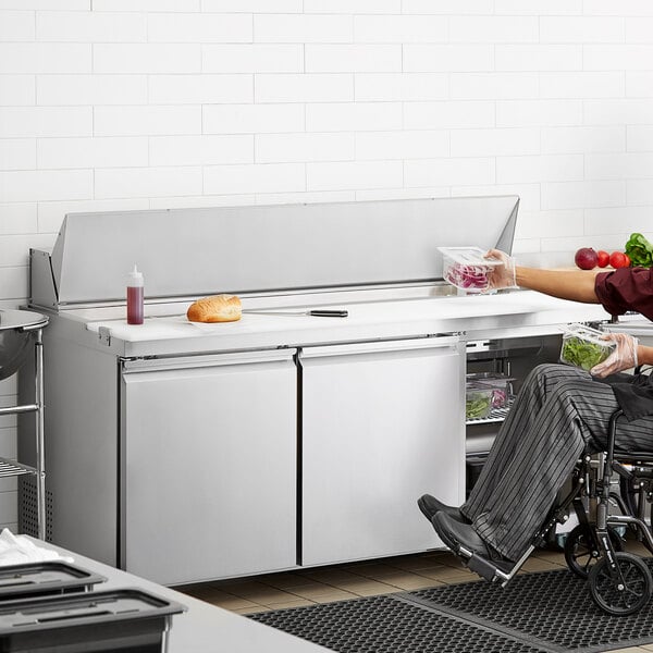 A man in a wheelchair using an Avantco stainless steel sandwich prep table in a professional kitchen.