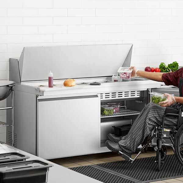 A man in a wheelchair at a stainless steel ADA height Avantco sandwich prep table.