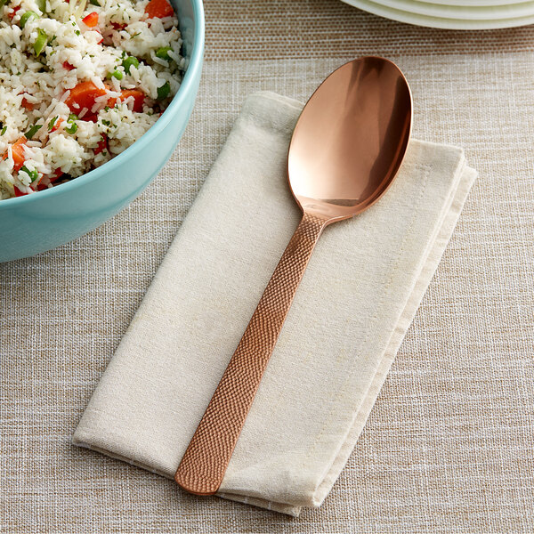 A close-up of an American Metalcraft hammered bronze serving spoon next to a bowl of rice.