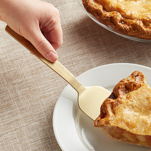 A hand holding an American Metalcraft hammered gold pie server over a slice of pie.