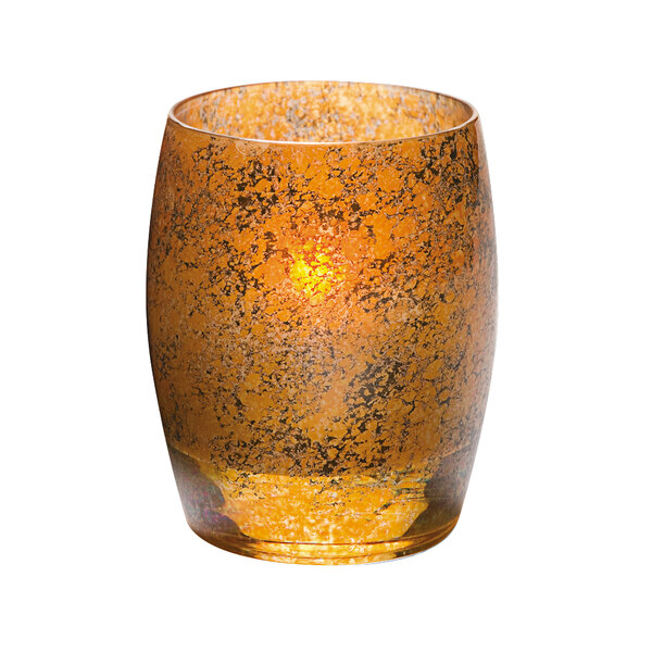 A Hollowick glass votive candle holder with an antique gold finish holding a lit candle.
