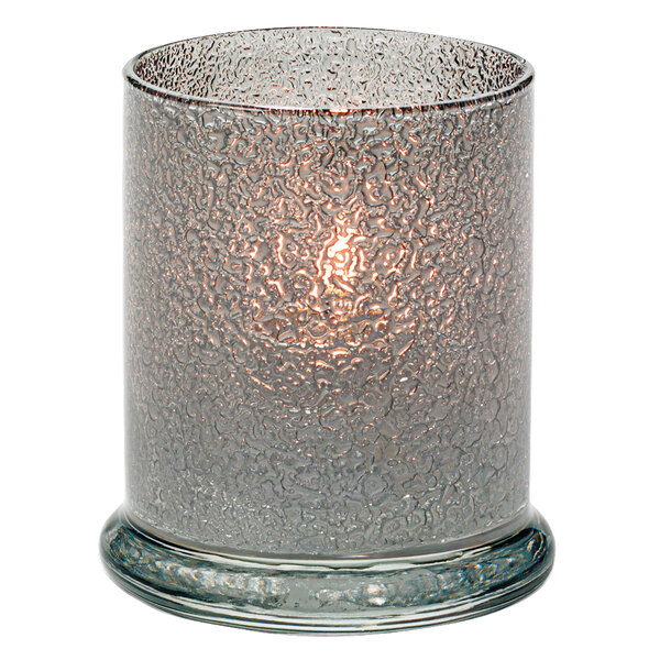 A lit Hollowick Smoke Jewel glass candle holder on an outdoor patio.