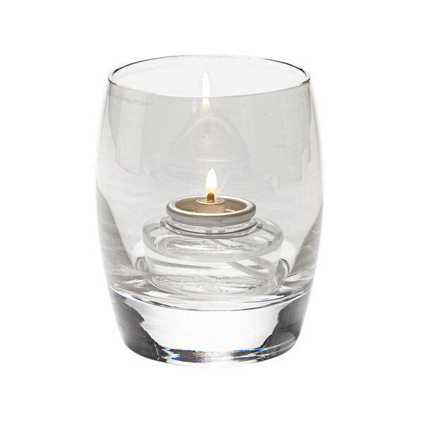 A clear glass Hollowick votive with a lit candle inside.